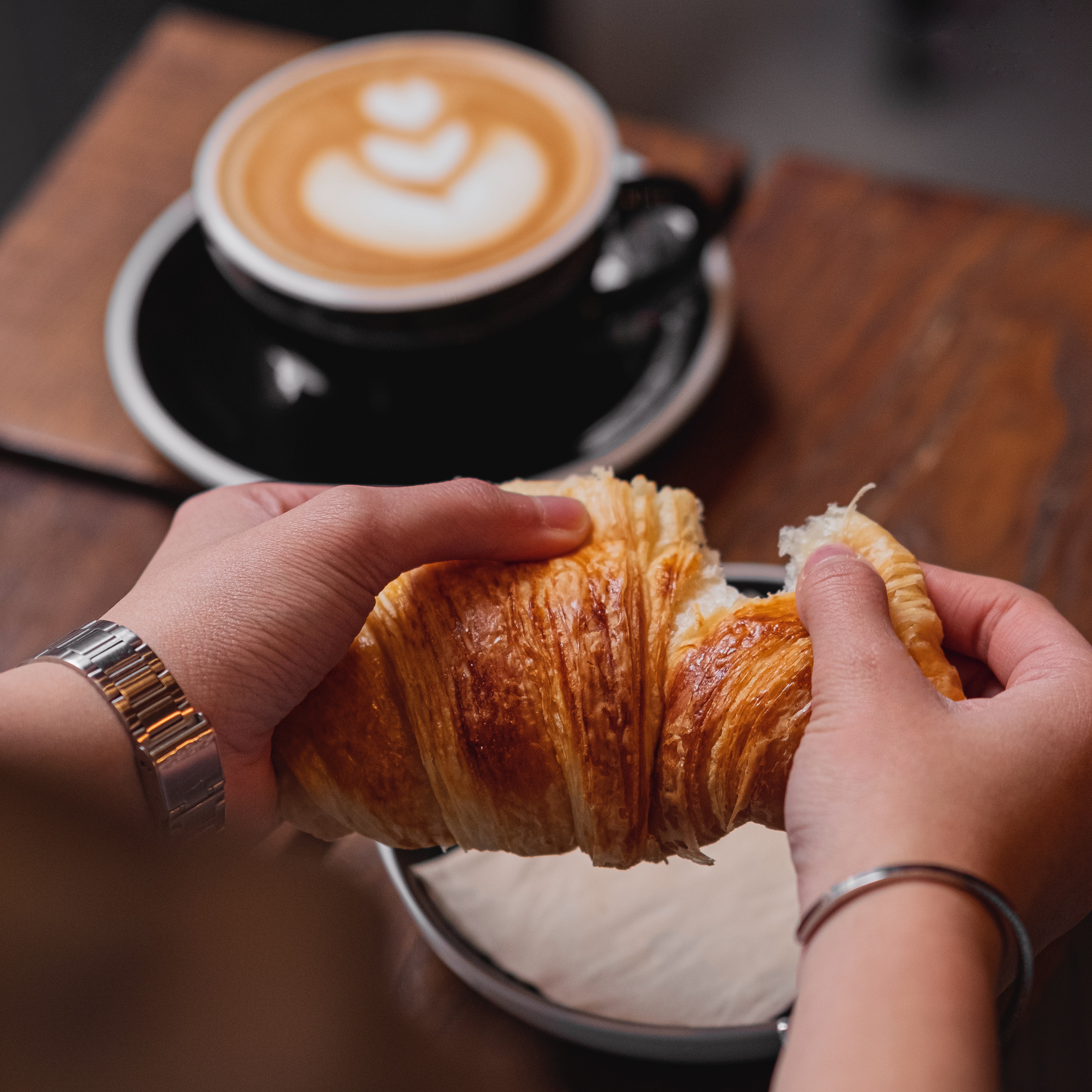 it's a photo of a person eating a croissant with a coffee cup on a table